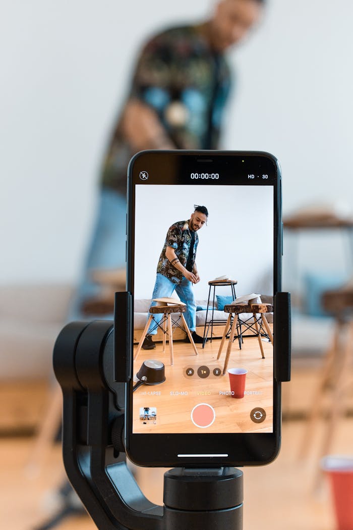 A person filming content using a smartphone and tripod setup indoors.