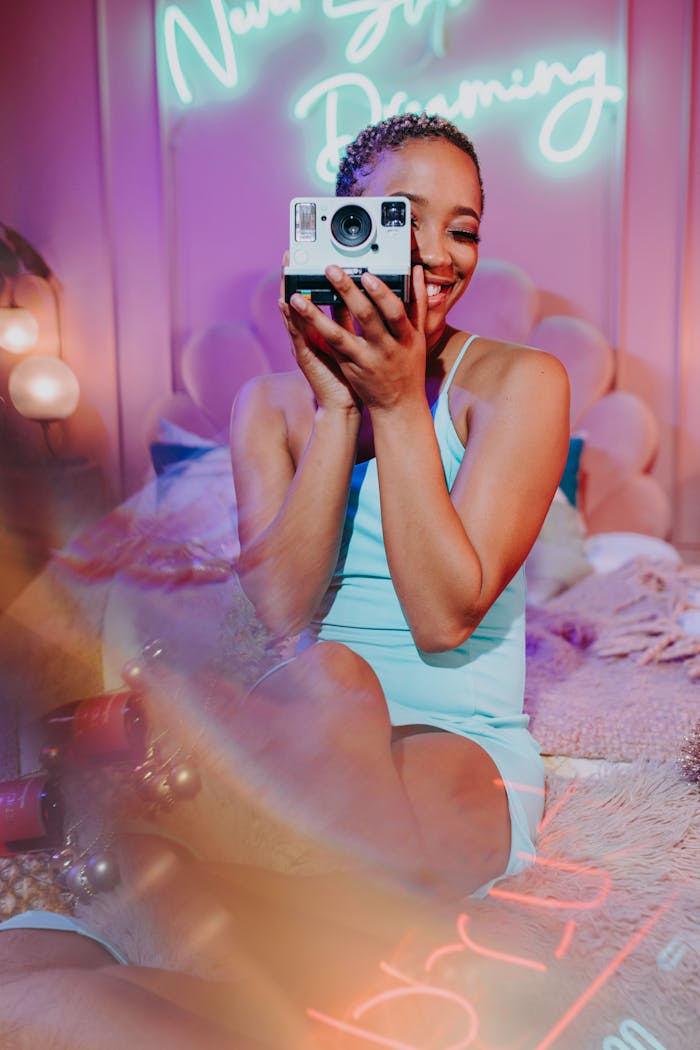 Smiling woman holding a camera in a cozy, softly lit room with neon text.